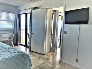 A hotel room with a bed, a desk, a chair, a TV, and a sliding door leading to an outdoor area. - Oceanfront Top-Floor Corner Unit, Fishing Pier & Pool at Amelia By The Sea (Fernandina Beach)