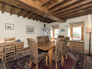 A dining area with a wooden table, four chairs, a bookshelf, and a window with a view.
