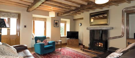 Una sala acogedora con chimenea, sofás de cuero, un sillón azul y una alfombra roja estampada.