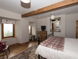 Quarto com teto de madeira, cama com manta xadrez, televisão em uma cômoda e janela com cortina.