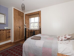 A bedroom with a bed, a wooden wardrobe, a mirror, and a window with blinds.