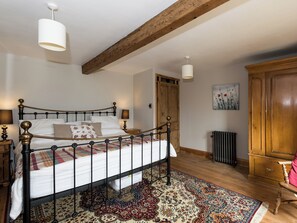 A bedroom with a bed, wooden beams, a radiator, a wardrobe, and a rug.