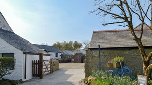 Un chemin de gravier mène à des cottages bordés d’un mur de pierres et sur lequel est apposée une pancarte indiquant « HALLAGENNA COTTAGES ».