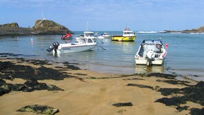 Une zone côtière où des bateaux sont amarrés près d’une plage de sable où l’on trouve des algues.