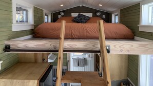 A loft-style bedroom with a bunk bed, wooden ladder, and a small kitchenette below.