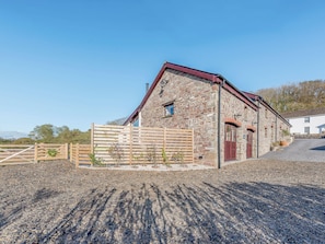 A stone building with a red roof, a wooden gate, and a gravel driveway.