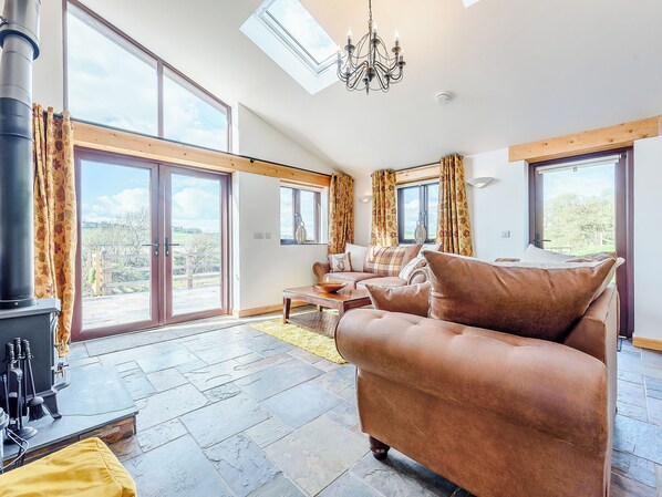 A spacious living room with a large sofa, a fireplace, and large windows offering a view of the outdoors.