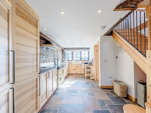 A kitchen with wooden cabinets, a stone floor, and a view to the dining area.