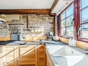A kitchen with stone walls, wooden beams, a coffee maker, and a window with a view.