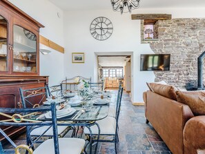 A dining area with a table set for four, a wooden cabinet with glass doors, a stone wall with a fireplace, and a brown leather sofa.