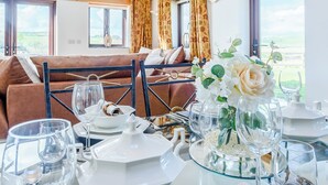 Un área de comedor con una mesa dispuesta para tomar el té, un sofá al fondo y vistas del exterior a través de amplias ventanas.