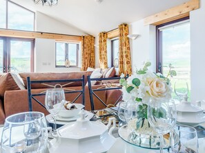 A dining area with a table set for tea, a sofa in the background, and a view of the outdoors through large windows.