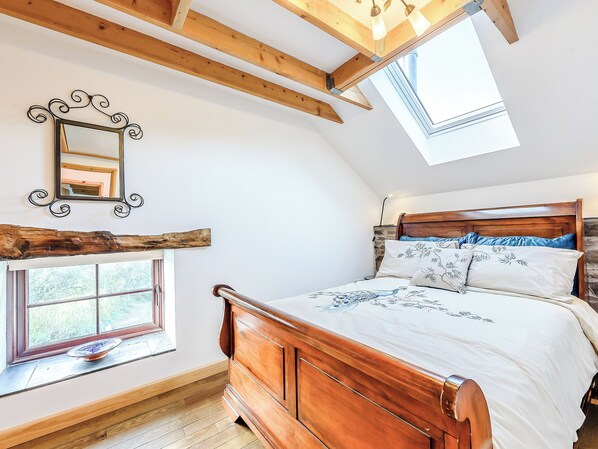 A bedroom with a wooden bed, a skylight, a window, and a mirror.