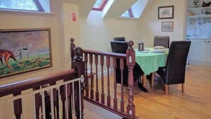 A dining area with a table set for two, a staircase with a wooden railing, and a painting on the wall. - 1 bedroom accommodation in Tatterford Hall, near Fakenham (Tatterford Hall, near Fakenham)