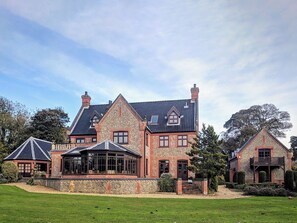Una casa grande de dos pisos con fachada de piedra, varios chimeneas y un césped bien cuidado.