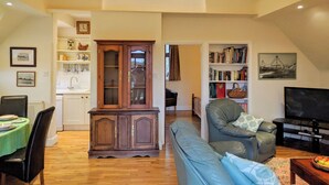 A spacious living room with a high ceiling, a dining area with a green tablecloth, a wooden cabinet, and a bookshelf filled with books. - 1 bedroom accommodation in Tatterford Hall, near Fakenham (Tatterford Hall, near Fakenham)