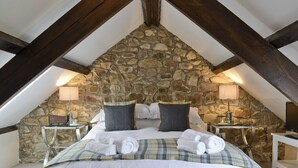 A cozy bedroom with a stone wall, a wooden ceiling, a bed with white linens, two bedside tables with lamps, and a wooden bench. - 1 bedroom accommodation in Marros, near Amroth (Marros, near Amroth)