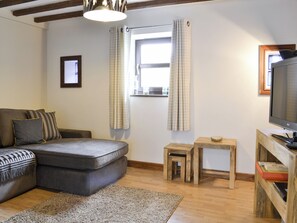 Una sala de estar con un sofá seccional gris, una mesita de madera, un televisor sobre un mueble de madera y una ventana con cortinas.