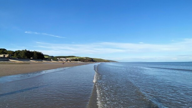 A beach with a clear sky, calm water, and a distant view of a town with buildings and greenery. - 1 bedroom accommodation in Marros, near Amroth (Marros, near Amroth)
