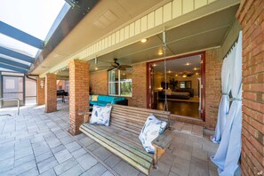 A covered patio with a wooden bench, a ceiling fan, and a brick wall.