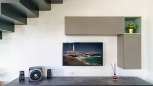 A modern living room with a large flat-screen TV mounted on the wall, a dark wooden cabinet below, and a staircase to the left. - Villa Vittoria - Waterfront house (Augusta)
