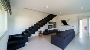 A modern living room with a black staircase, a grey sofa, and a flat-screen TV on a black stand. - Villa Vittoria - Waterfront house (Augusta)
