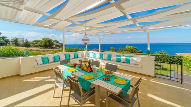 An outdoor dining area with a view of the sea, a white ceiling, and a table set with plates, glasses, and fruits. - Villa Vittoria - Waterfront house (Augusta)