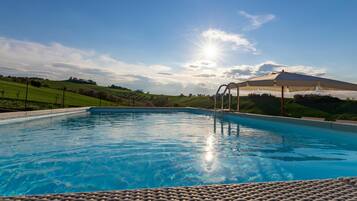Relax by the serene pool surrounded by lush green hills and a clear sky.