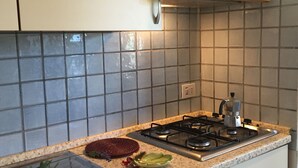 A kitchen with a gas stove, a coffee maker, and a tray with vegetables and flowers on the counter. - Casa Ibiscus 1 Bedrooms Apartment in Stintino (Stintino)
