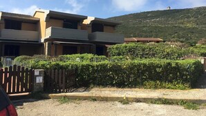 A residential building with a two-story structure, a balcony, and a view of a hill with a tower in the distance. - Casa Ibiscus 1 Bedrooms Apartment in Stintino (Stintino)