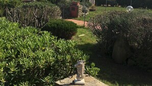 A garden with a statue, a car, and a building in the background. - Casa Ibiscus 1 Bedrooms Apartment in Stintino (Stintino)