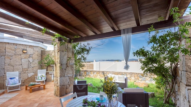 Un patio exterior con paredes de piedra, un pérgola de madera y vista al mar.
