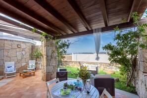 An outdoor patio with stone walls, a wooden pergola, and a view of the sea. - Villino Coralla 2 Bedrooms Apartment in Alghero (Alghero)