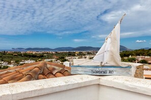 A sailboat named "Sardinia Re" on a rooftop with a cityscape and mountains in the background.