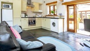 Une cuisine moderne équipée d’un four, d’un micro-ondes et d’un lave-linge intégrés, un coin repas avec un canapé en cuir noir et une vue sur l’extérieur grâce à une porte vitrée.