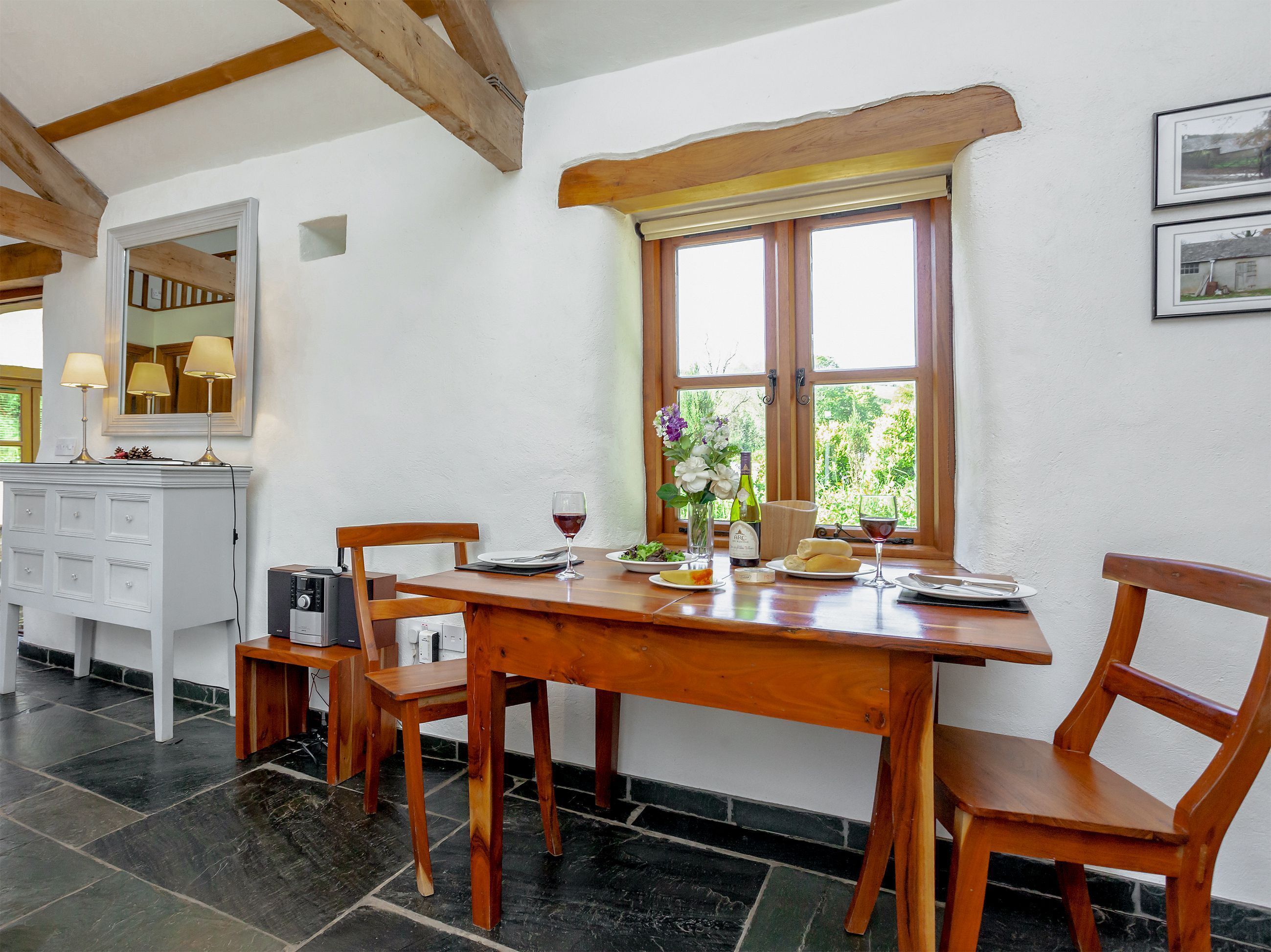 Un coin repas avec une table en bois, des chaises et une fenêtre donnant sur un paysage verdoyant. On y trouve également un meuble blanc avec des tiroirs et un miroir au-dessus.