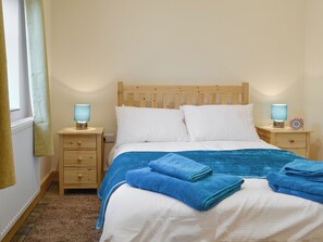 Ein Schlafzimmer mit einem hölzernen Kopfende, zwei Nachttischen mit Lampen, einem Bett mit weißen Bettwäsche und blauen Handtüchern sowie einem Fenster mit Vorhängen.