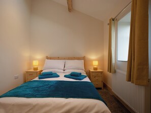 A single bed with a wooden headboard, two bedside tables with lamps, a window with curtains, and a teal throw blanket.