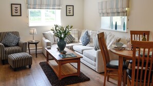 A living room with a sofa, two armchairs, a coffee table, a dining table with chairs, a vase with flowers, and a window with curtains. - 2 bedroom accommodation in Brampton, near Carlisle (Brampton, near Carlisle)