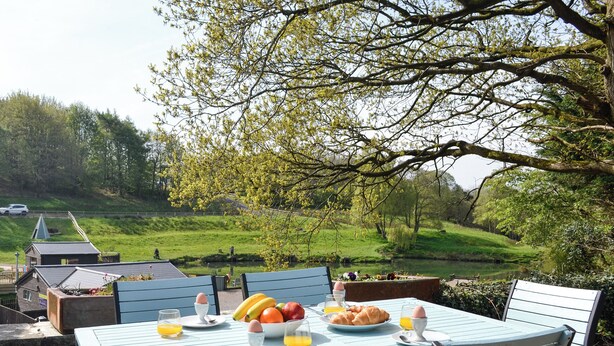 A table set with breakfast items, surrounded by chairs, overlooking a scenic landscape with a lake and greenery. - 2 bedroom accommodation in Brampton, near Carlisle (Brampton, near Carlisle)