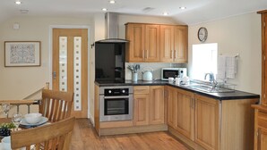 A kitchen with wooden cabinets, a stove, oven, microwave, and a dining area with a table and chairs. - 2 bedroom accommodation in Brampton, near Carlisle (Brampton, near Carlisle)
