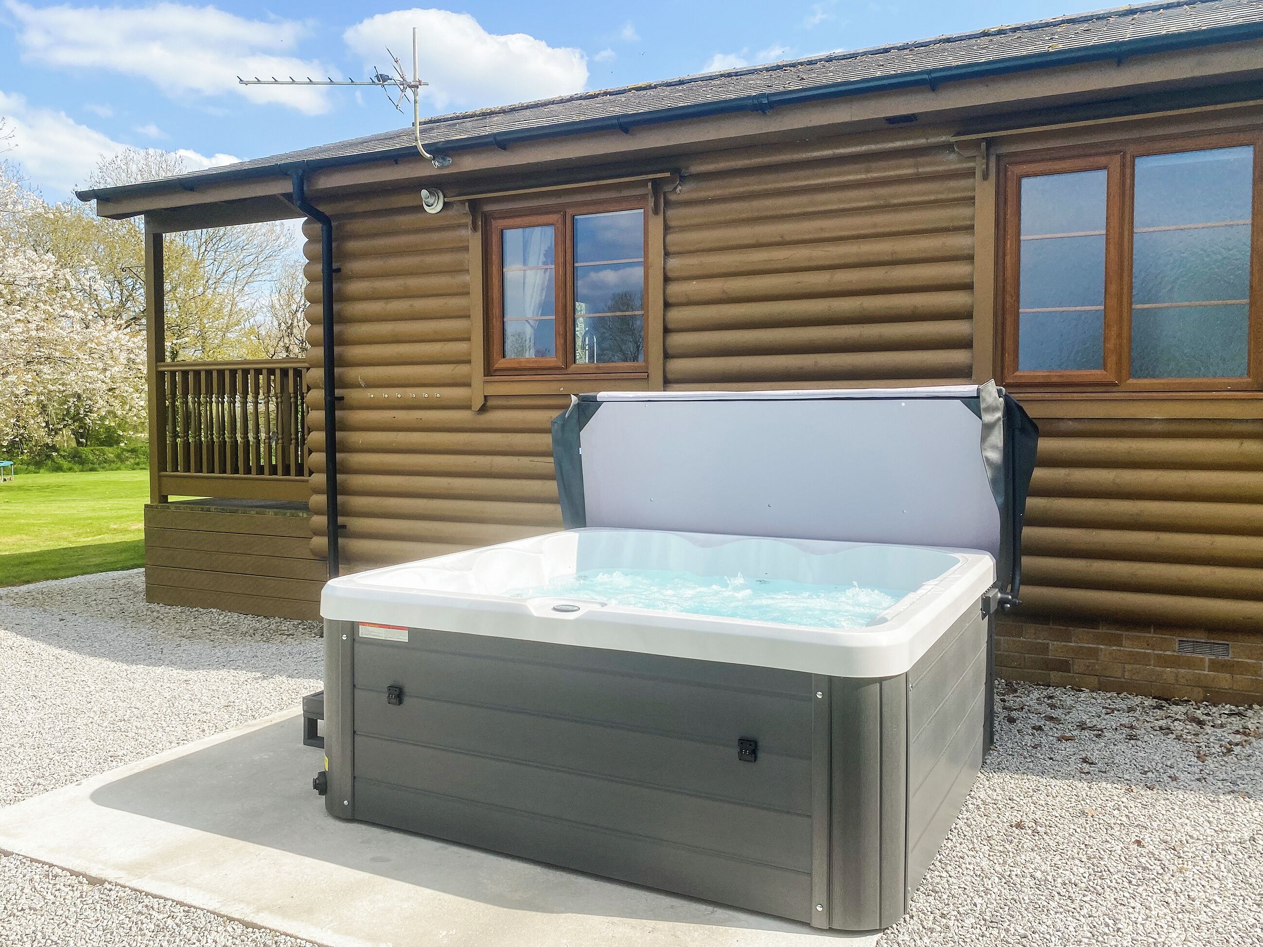 Een hottub voor een blokhut met een houten terras en een raam.