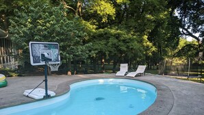 Ein Swimmingpool mit Basketballkorb, Liegestühlen und einem Zaun.