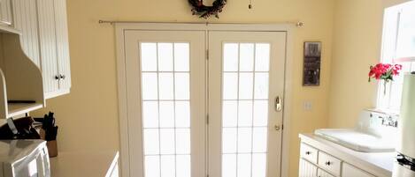 A kitchen with white cabinets, a double door entrance, a ceiling fan, and a window with a flower vase.