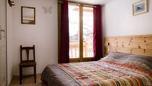 A bedroom with a wooden bed, a chair, a window with curtains, and a framed picture on the wall.