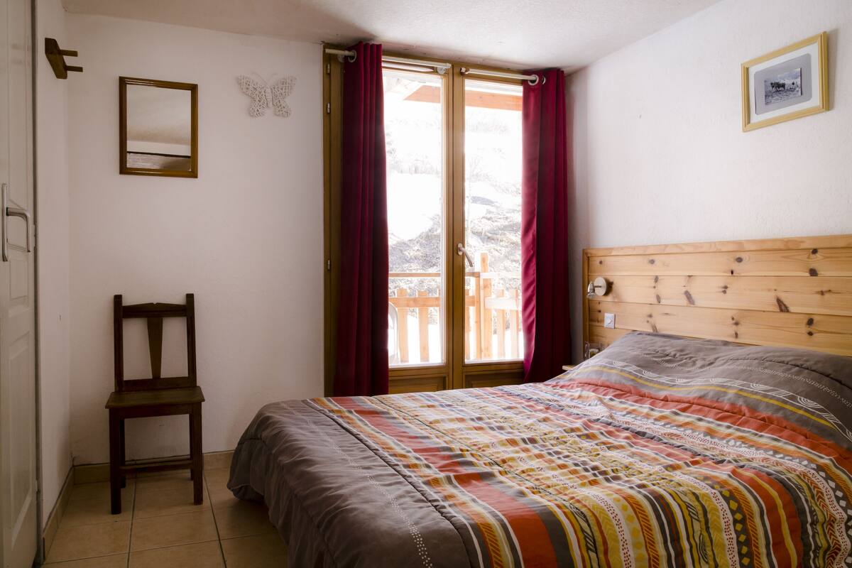 Une chambre à coucher avec un lit en bois, une chaise, une fenêtre avec des rideaux et un tableau encadré au mur.