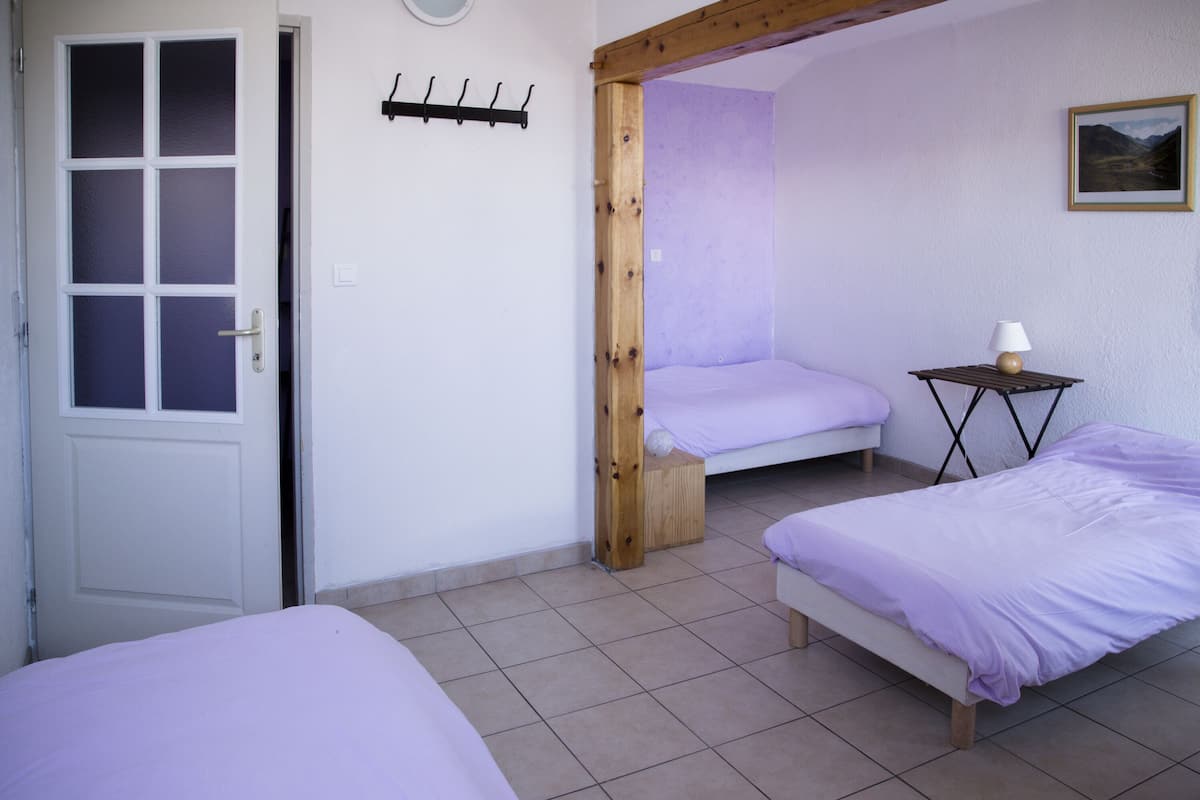Une chambre avec deux lits, une porte en bois, un porte-manteau fixé au mur et une petite table avec une lampe.