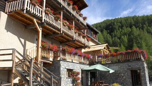 A chalet with wooden balconies adorned with flower boxes, a stone facade, and a stone entrance.