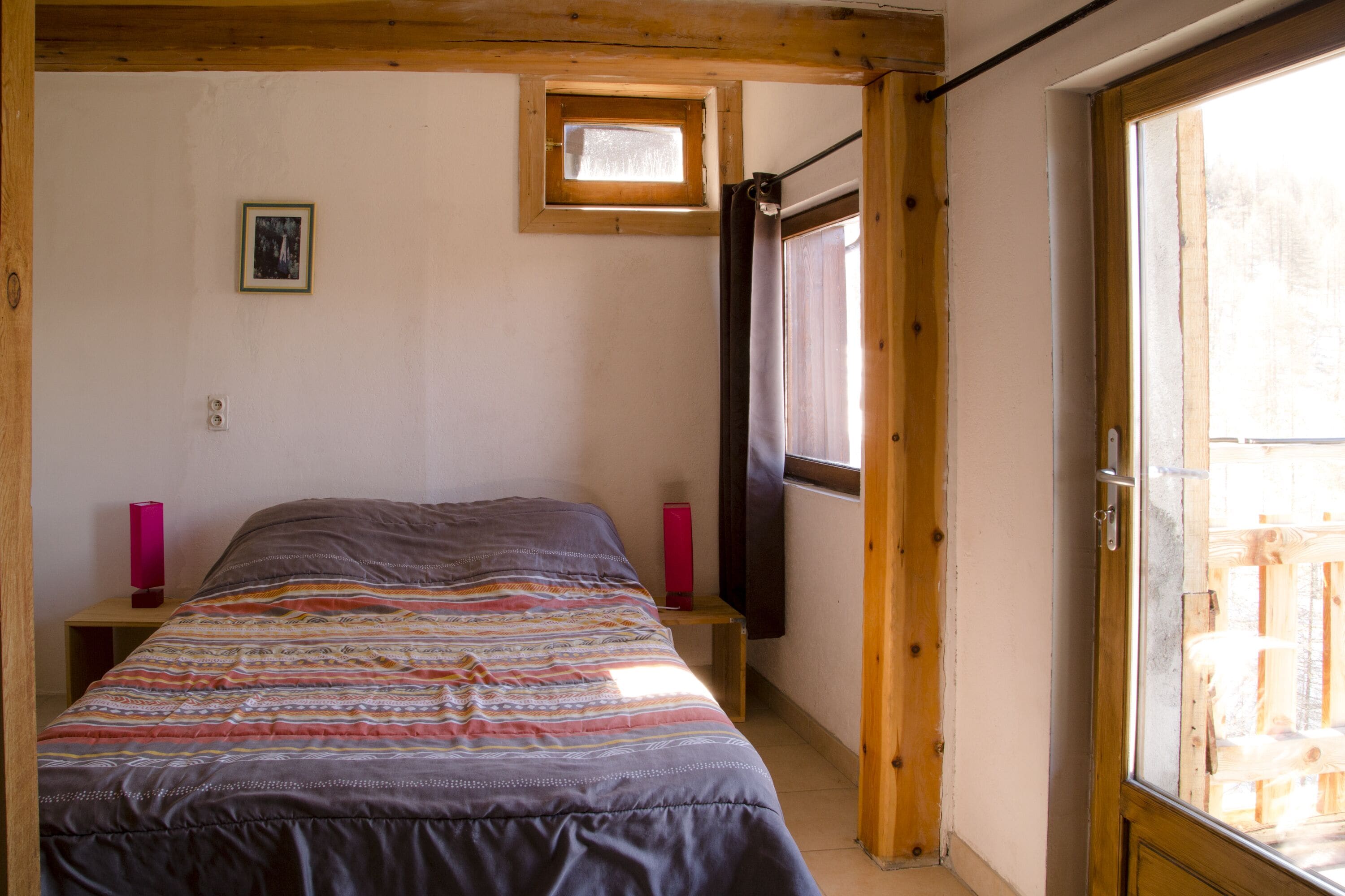 A bedroom with a bed, a small window, a door, and a picture on the wall.