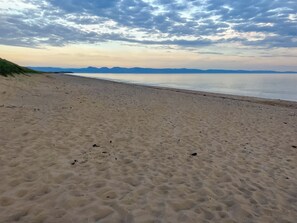 Une plage de sable fin, avec un ciel dégagé et des montagnes à l’horizon.